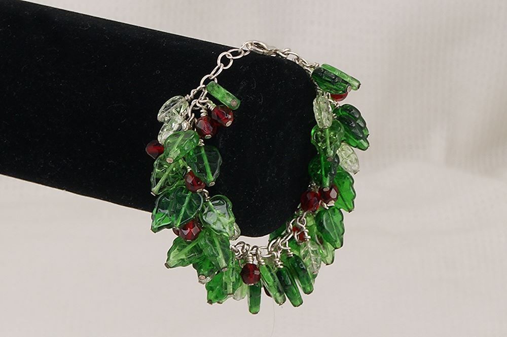 One of a kind bracelet with red and green glass holly leaves and berries .